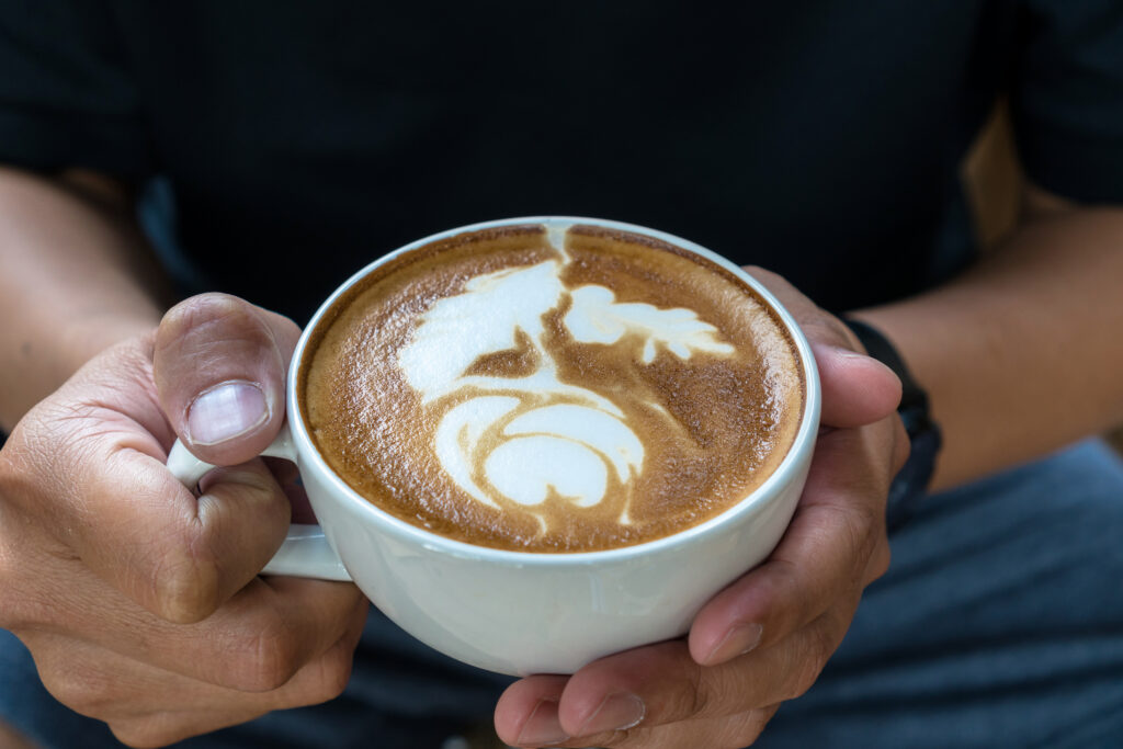 Closeup man hand holding the cup of coffee with latte art, art a